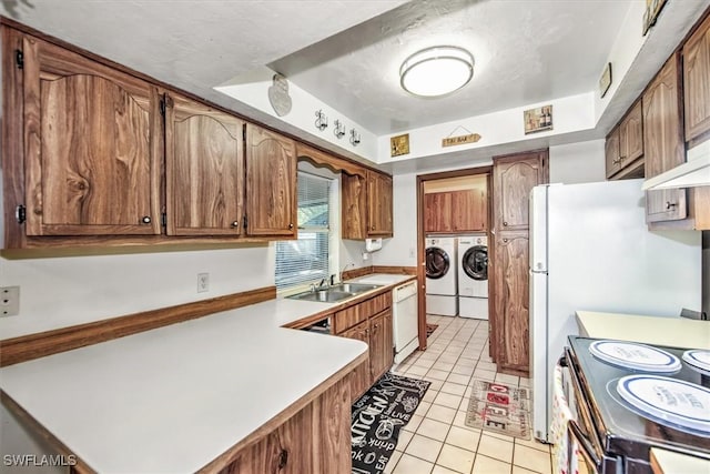 kitchen with white appliances, light tile patterned floors, brown cabinetry, washing machine and clothes dryer, and a sink