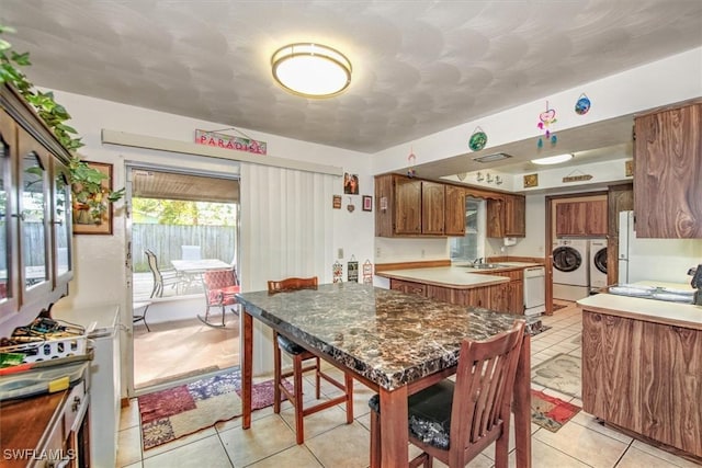 kitchen with brown cabinets, washing machine and clothes dryer, light tile patterned floors, a sink, and dishwasher