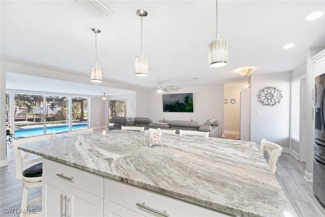 kitchen featuring ceiling fan, light hardwood / wood-style floors, light stone counters, white cabinetry, and a breakfast bar area