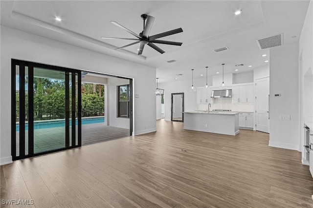 unfurnished living room with a tray ceiling, ceiling fan, sink, and light wood-type flooring