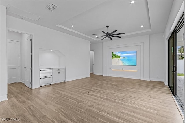 unfurnished living room with a tray ceiling, ceiling fan, and light hardwood / wood-style flooring