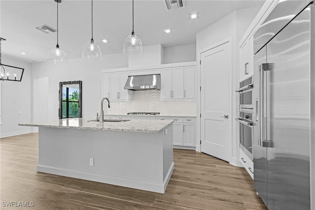 kitchen with white cabinets, a center island with sink, wall chimney exhaust hood, and built in fridge