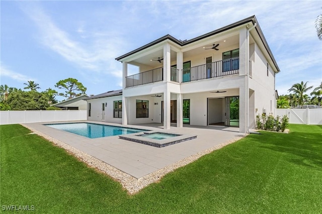 back of house featuring a lawn, ceiling fan, a swimming pool with hot tub, a balcony, and a patio