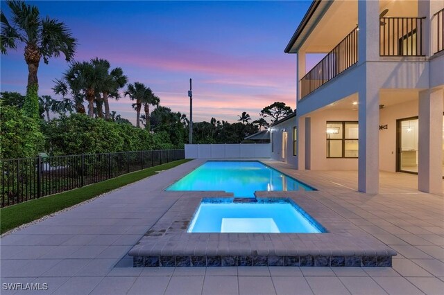 pool at dusk with an in ground hot tub and a patio area