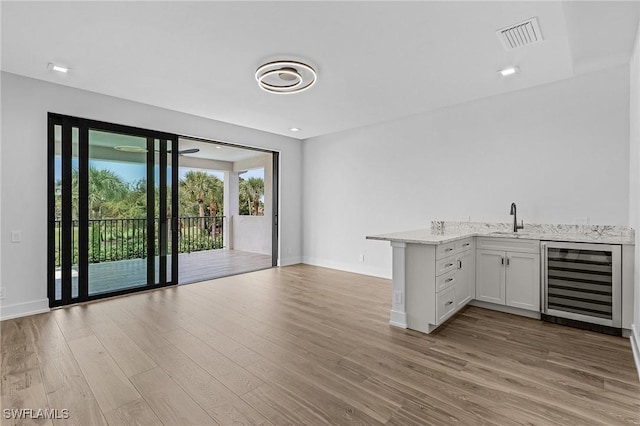 kitchen with sink, white cabinets, beverage cooler, and light wood-type flooring