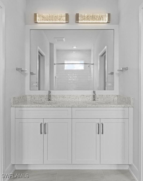 full bath featuring tiled shower, double vanity, and a sink