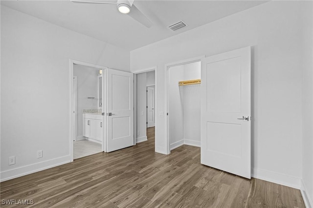 unfurnished bedroom with hardwood / wood-style floors, ceiling fan, a closet, and ensuite bath