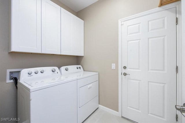 clothes washing area featuring cabinets, light tile patterned flooring, and washing machine and dryer