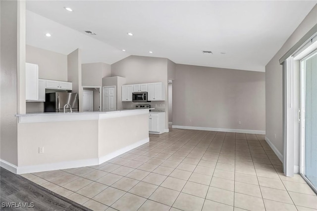 kitchen with white cabinets, vaulted ceiling, light tile patterned floors, kitchen peninsula, and stainless steel appliances