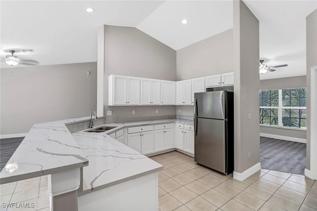 kitchen featuring ceiling fan, light stone countertops, kitchen peninsula, stainless steel fridge, and vaulted ceiling