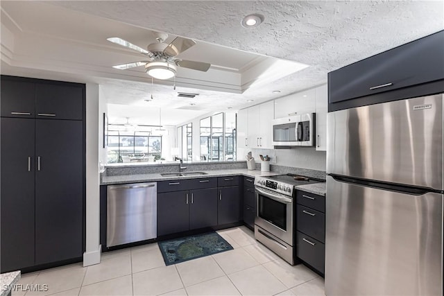 kitchen featuring a textured ceiling, a tray ceiling, appliances with stainless steel finishes, ceiling fan, and sink