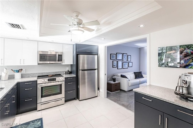 kitchen with appliances with stainless steel finishes, ceiling fan, light stone counters, a tray ceiling, and white cabinetry