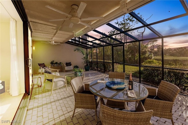 patio terrace at dusk featuring ceiling fan and glass enclosure