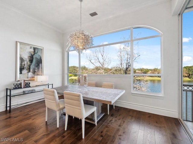 dining room with dark wood-type flooring, a water view, crown molding, and a chandelier