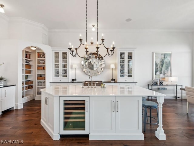 kitchen featuring wine cooler, white cabinetry, crown molding, and an island with sink