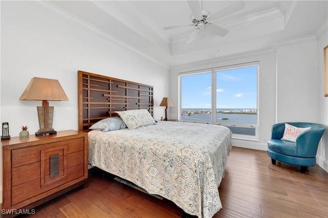 bedroom featuring ceiling fan, crown molding, hardwood / wood-style floors, a tray ceiling, and a water view