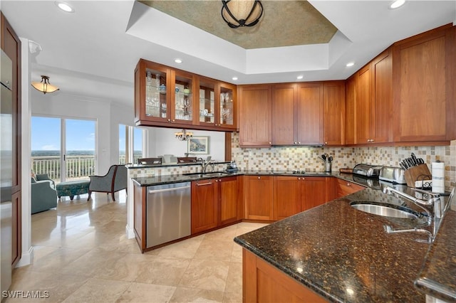 kitchen with dishwasher, a tray ceiling, dark stone countertops, and sink