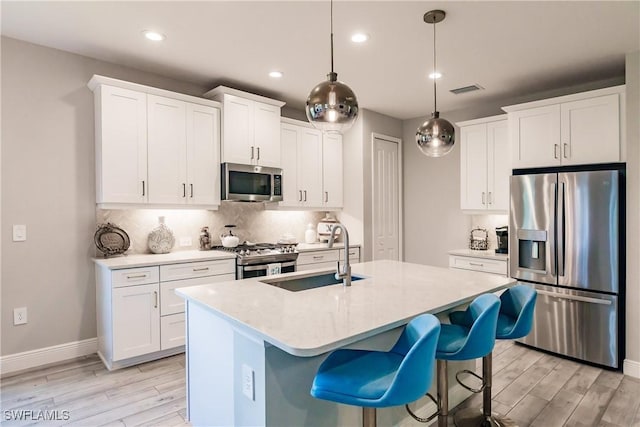 kitchen with white cabinetry, sink, hanging light fixtures, an island with sink, and appliances with stainless steel finishes