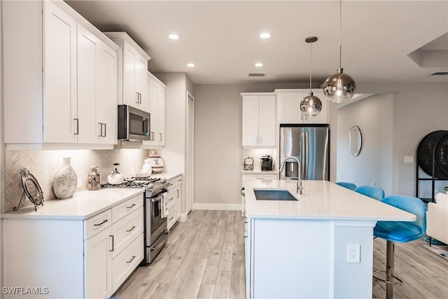 kitchen with a kitchen breakfast bar, sink, hanging light fixtures, appliances with stainless steel finishes, and white cabinetry