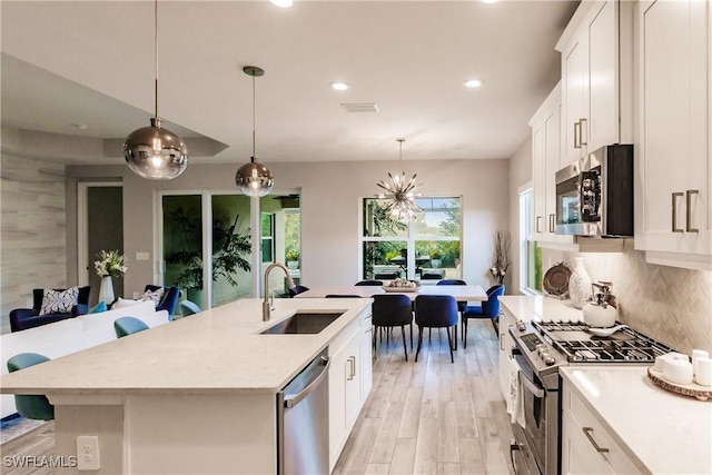 kitchen featuring backsplash, stainless steel appliances, a kitchen island with sink, decorative light fixtures, and white cabinets