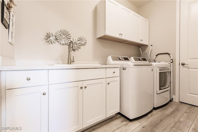 laundry area featuring cabinets, independent washer and dryer, sink, and light hardwood / wood-style flooring