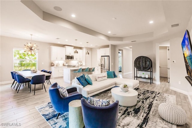 living room featuring a tray ceiling, a chandelier, and light wood-type flooring