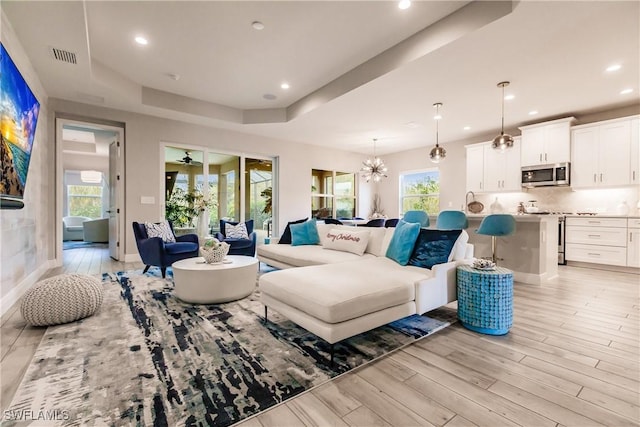 living room featuring a chandelier, light wood-type flooring, and a tray ceiling