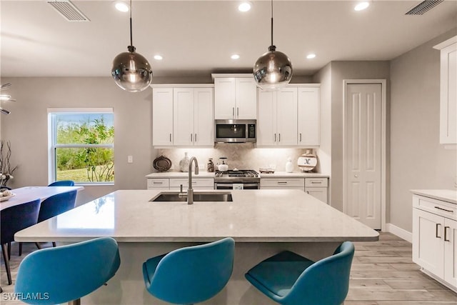 kitchen featuring sink, hanging light fixtures, appliances with stainless steel finishes, white cabinets, and light wood-type flooring