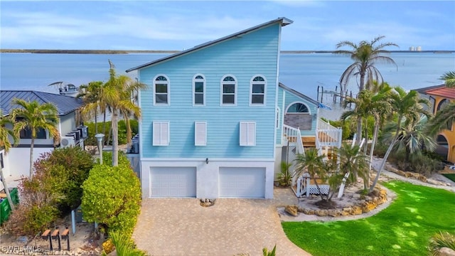 beach home featuring a garage, stairway, a water view, decorative driveway, and stucco siding
