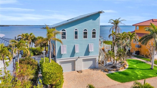 raised beach house with an attached garage, central AC, a water view, decorative driveway, and a front yard