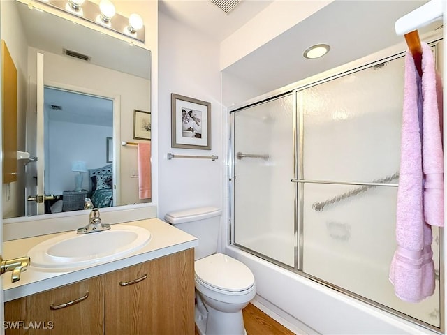 full bathroom featuring shower / bath combination with glass door, vanity, hardwood / wood-style flooring, and toilet