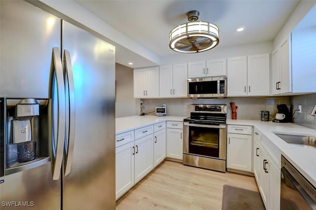 kitchen featuring white cabinetry, sink, backsplash, appliances with stainless steel finishes, and light wood-type flooring