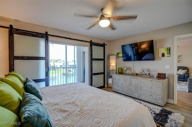 bedroom featuring access to exterior, light wood-type flooring, a barn door, and ceiling fan