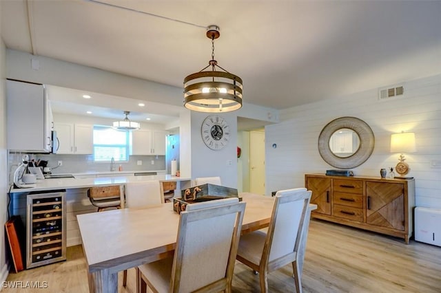 dining room with wooden walls, light hardwood / wood-style flooring, beverage cooler, and sink