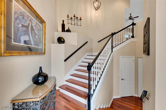 stairway with ceiling fan, a towering ceiling, and hardwood / wood-style flooring