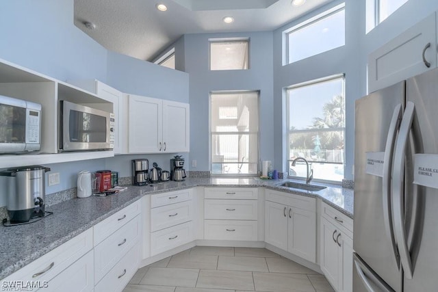 kitchen with white cabinets, white microwave, light stone counters, freestanding refrigerator, and a sink