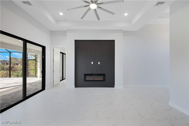 empty room with ceiling fan, a large fireplace, and a tray ceiling