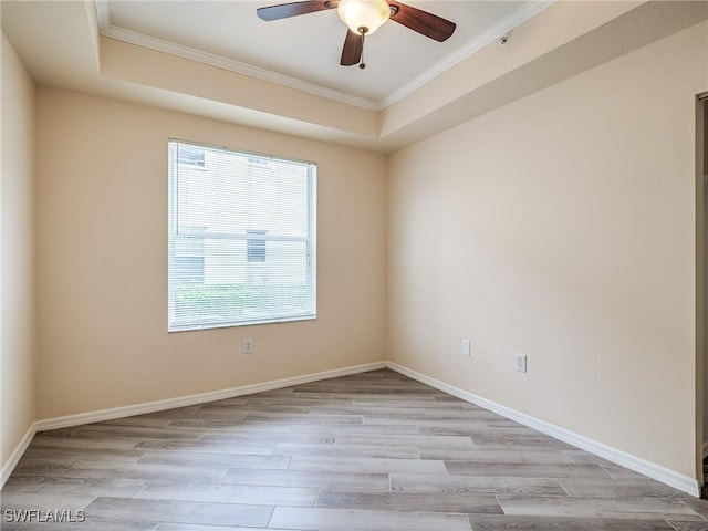 spare room with a tray ceiling, crown molding, ceiling fan, and light wood-type flooring