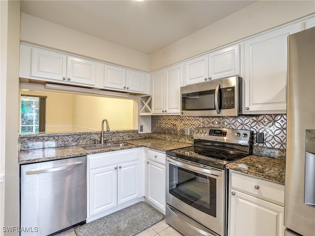 kitchen featuring sink, stainless steel appliances, white cabinets, dark stone counters, and light tile patterned flooring