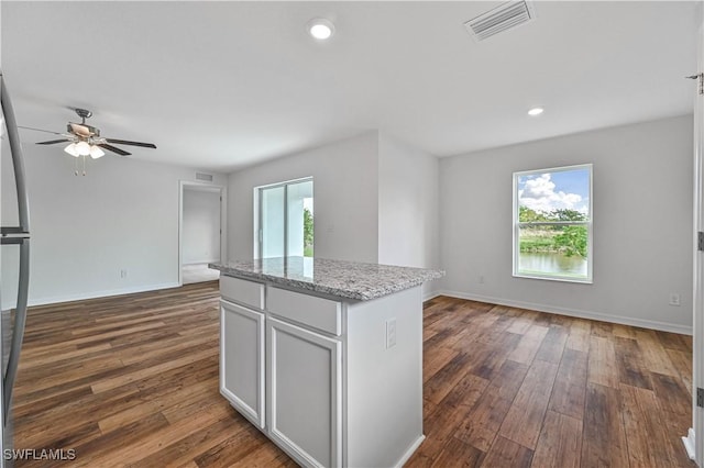 kitchen with white cabinetry, ceiling fan, light stone counters, dark hardwood / wood-style floors, and a kitchen island