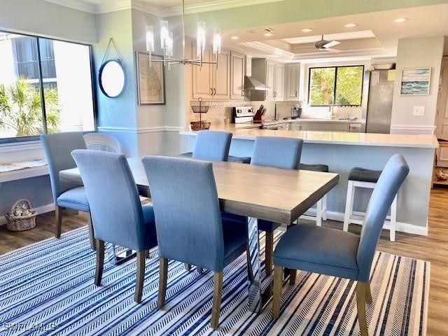 dining space featuring a raised ceiling, ornamental molding, a chandelier, and light hardwood / wood-style floors