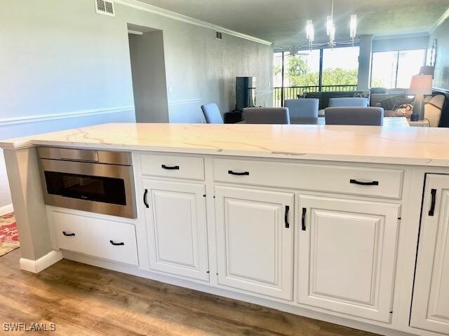 kitchen with white cabinetry, an inviting chandelier, decorative light fixtures, light stone countertops, and light hardwood / wood-style floors