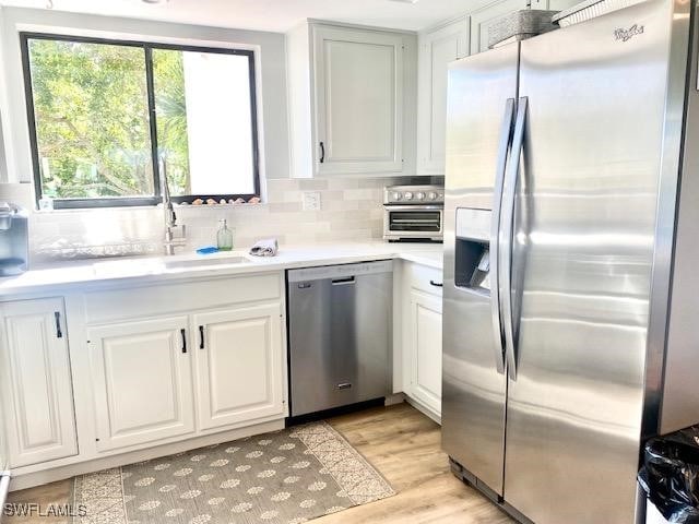 kitchen with sink, white cabinetry, tasteful backsplash, light wood-type flooring, and stainless steel appliances