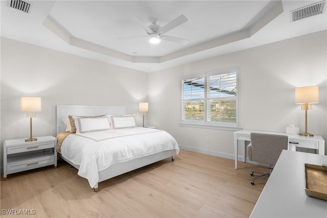 bedroom with a tray ceiling, ceiling fan, and light hardwood / wood-style flooring