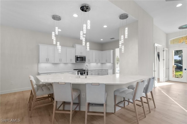 kitchen with a kitchen bar, appliances with stainless steel finishes, light wood-type flooring, decorative light fixtures, and white cabinetry