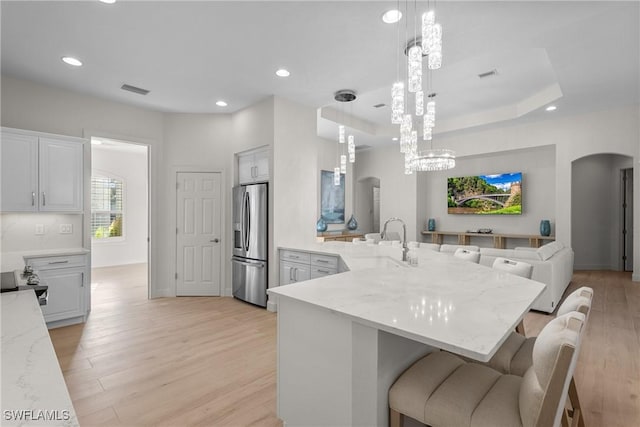 kitchen with a breakfast bar, sink, stainless steel refrigerator with ice dispenser, and hanging light fixtures