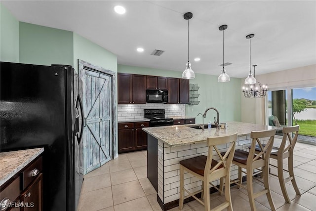 kitchen with a breakfast bar, black appliances, a center island with sink, sink, and decorative light fixtures