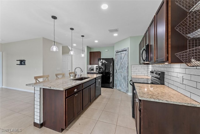 kitchen with a breakfast bar, a kitchen island with sink, black appliances, hanging light fixtures, and sink