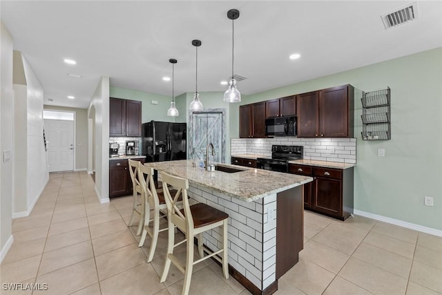 kitchen featuring light stone countertops, tasteful backsplash, a kitchen island with sink, black appliances, and sink