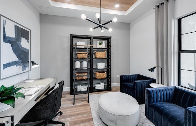 office with a tray ceiling, plenty of natural light, an inviting chandelier, and light wood-type flooring